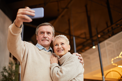 Below view of content handsome senior man with mustache using smartphone while posing with wife for selfie