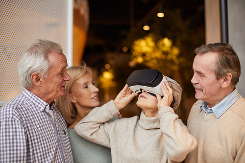 Seniors looking at woman using virtual reality device, curious woman in VR goggles looking around