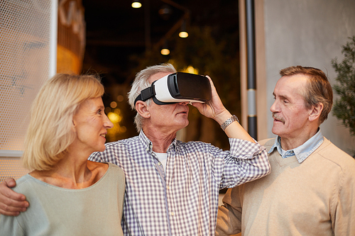Curious senior man adjusting virtual reality goggles and embracing wife while entering world of virtual reality