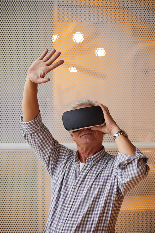 Modern handsome mature man with wristwatch wearing virtual reality headset waving hand