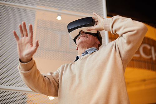 Below view of curious senior man with mustache gesturing hand while using virtual reality goggles