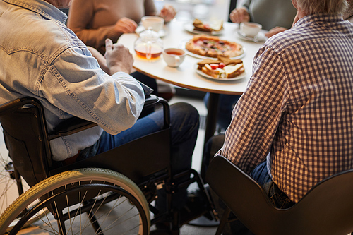 Close-up of unrecognizable handicapped man in wheelchair surrounded by friends sitting at table and chatting with friends