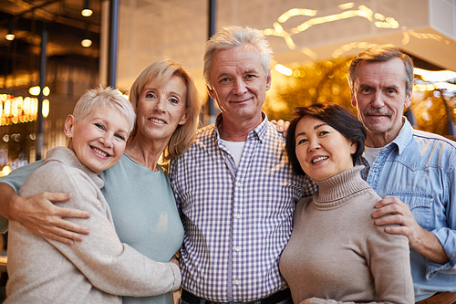 Group of cheerful senior multi-ethnic friends embracing each other while posing together for photo