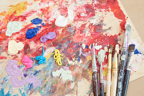 Close-up of palette with paints and different paintbrushes on the table in workshop