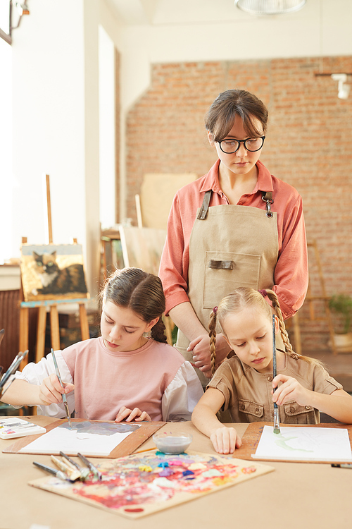 Young teacher standing and watching for the work of her students during art lesson in studio