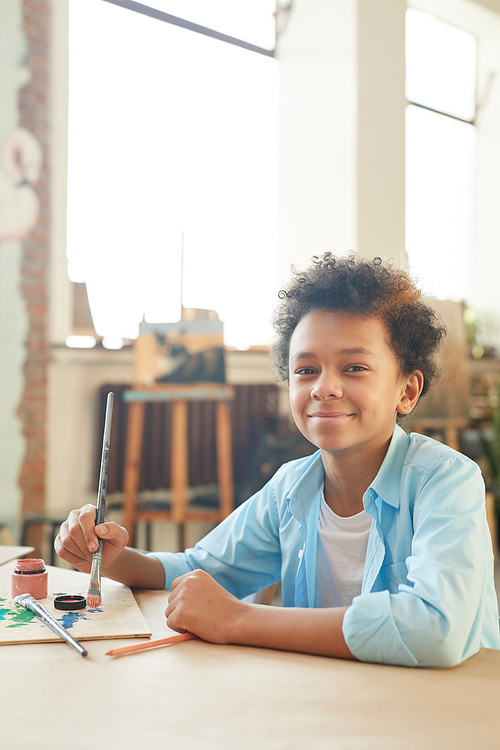 Portrait of African little boy looking at camera and painting a picture during his lesson at art studio