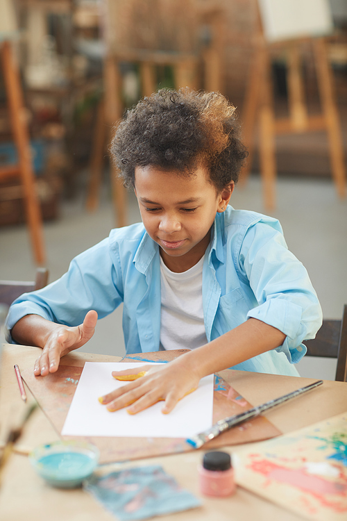 African little boy sitting at the table and making a handcraft with paints at art studio