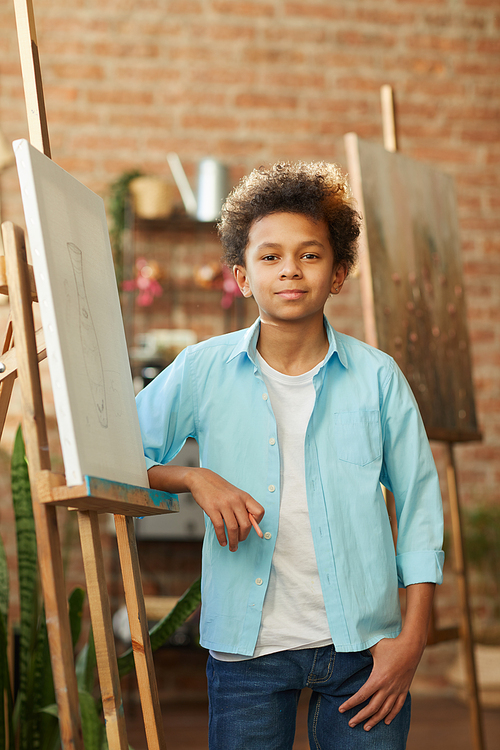 Portrait of African little boy standing near the easel and looking at camera at art studio