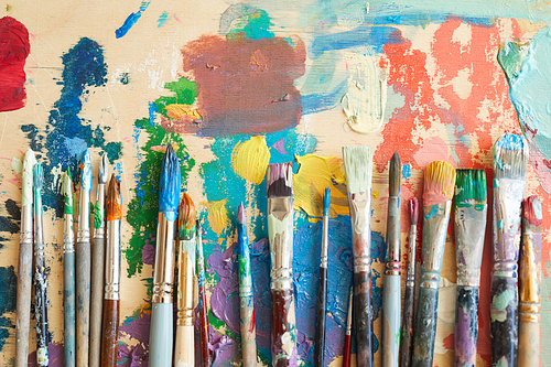 Close-up of different paintbrushes in paints lying on the painting