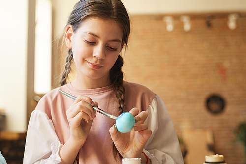 Cute girl painting an egg with paints she preparing for the Easter