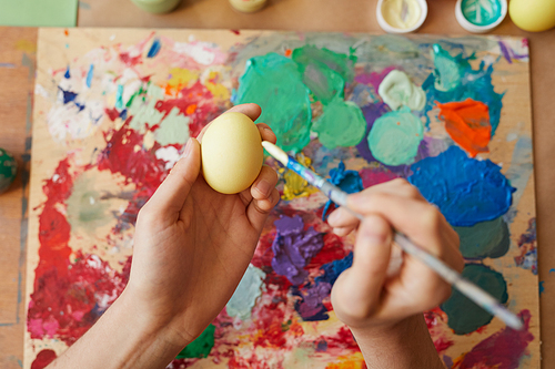 Close-up of female hands holding egg and decorating it with paints to holiday