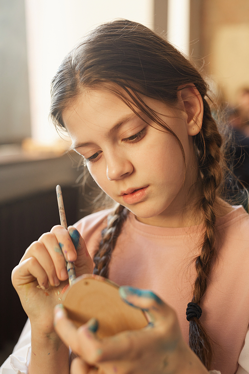 Serious girl concentrating on her craft work she holding a piece of wood and painting it with paintbrush