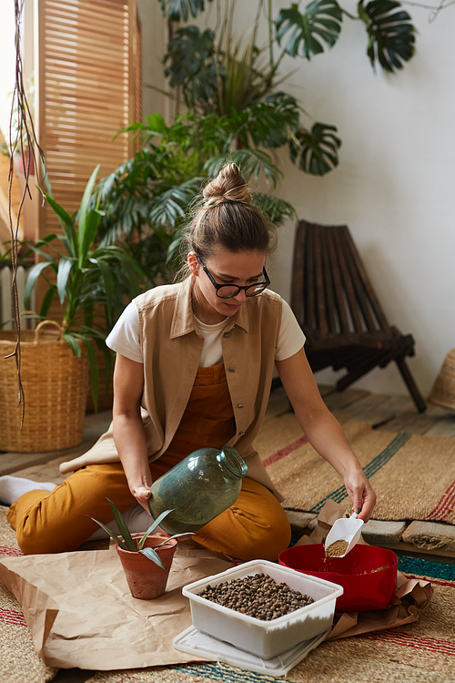 Young woman in eyeglasses sitting on the floor and preparing the ground to transplant the plant in the pot