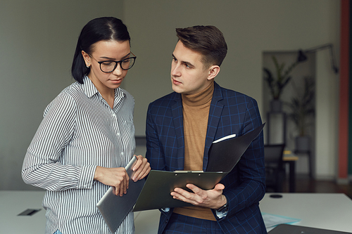 Young businessman showing some documents to businesswoman and they discussing them together at office