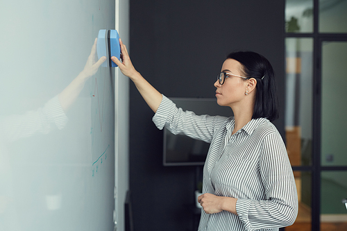 Young businesswoman wiping the whiteboard she preparing it for future presentation at office