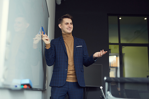 Young businessman pointing at whiteboard and presenting his report during presentation at office