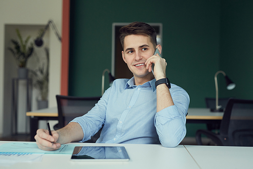 Young businessman has a consultation on mobile phone and working with documents at his workplace at office