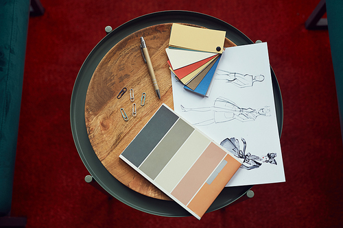 High angle view of design sketches and colored patterns lying on wooden table