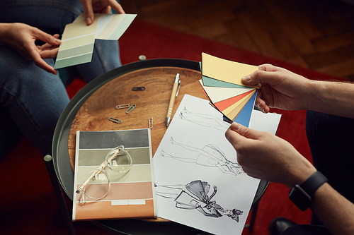 Close-up of team of designers looking at sketches and patterns and discussing new fashion collection together