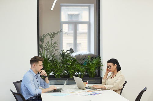 Young business colleagues sitting opposite each other at the table and working on laptop computers at office