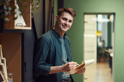 Portrait of young man smiling at camera while standing and examining contract in his hands