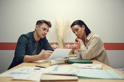 Businessman reading a document to businesswoman while they sitting at the table during meeting in cafe