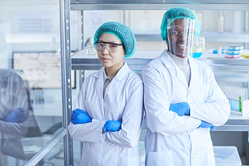 Portrait of man and woman in white coats and protective eyeglasses smiling at camera while working in the laboratory