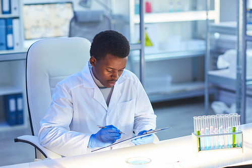 African young scientist sitting at the table and examining the medical card at his office