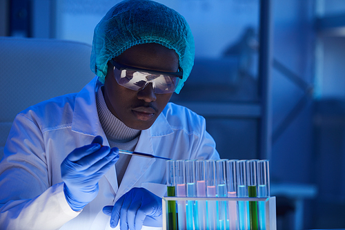 African scientist in protective workwear examining samples in test tubes in the lab