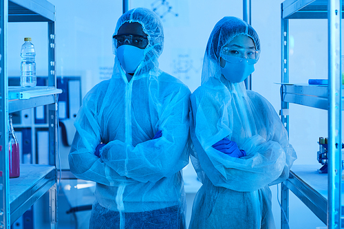 Portrait of two chemists in protective workwear standing with arms crossed and looking at camera in the laboratory