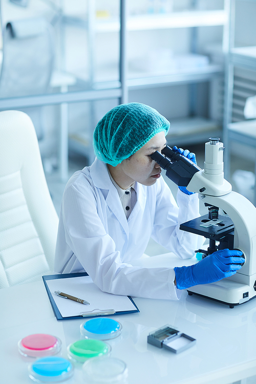 Female scientist sitting at her workplace and examining samples using microscope in the laboratory