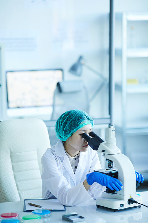 Female doctor sitting at her workplace and analyzing samples with microscope at the laboratory