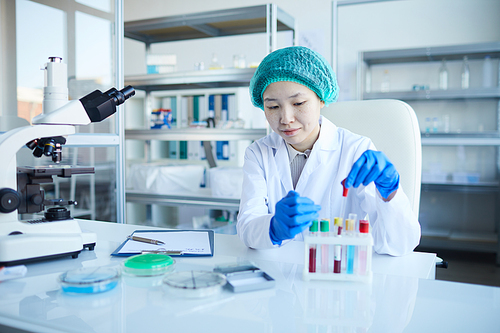 Asian nurse sitting at the table and examining the results of blood samples in the lab