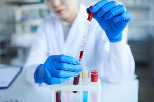 Close-up of female doctor in protective gloves examining the blood samples and working over analysis in the lab