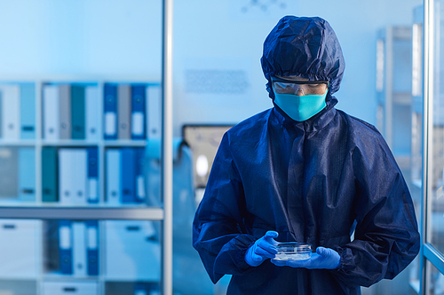 Doctor in protective costume and in mask examining the samples while working in the laboratory