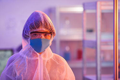 Portrait of nurse in protective clothing mask and glasses looking at camera while standing at office