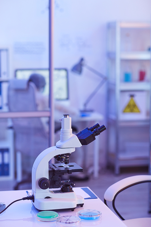 Close-up of microscope standing on the table with people working in the background at laboratory