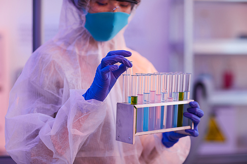 Close-up of woman in protective costume and protective gloves working with test tubes with colored liquid at the lab
