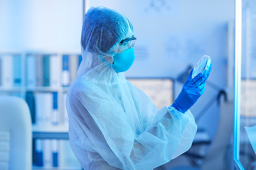 Medical worker in protective costume looking at samples in her hands while standing at medical laboratory