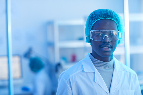 Portrait of African young doctor in white coat and in protective glasses looking at camera while working at office