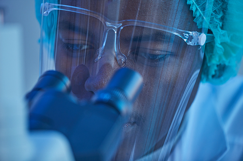 Close-up of African young man looking through the microscope during his work at the laboratory