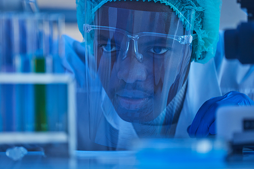 Close-up of African chemist in protective mask examining the samples in test tubes in the laboratory