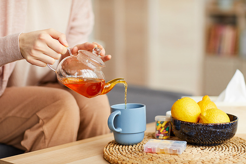 Close-up of young woman sitting on sofa and pouring tea into the cup at home