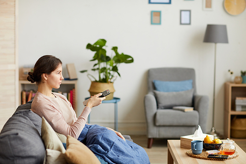 Young woman sitting on sofa with control remote and watching TV she has a cold and stay at home