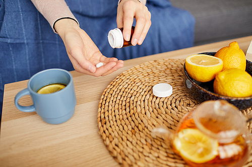 Close-up of woman taking vitamins and drinking tea with lemon at home