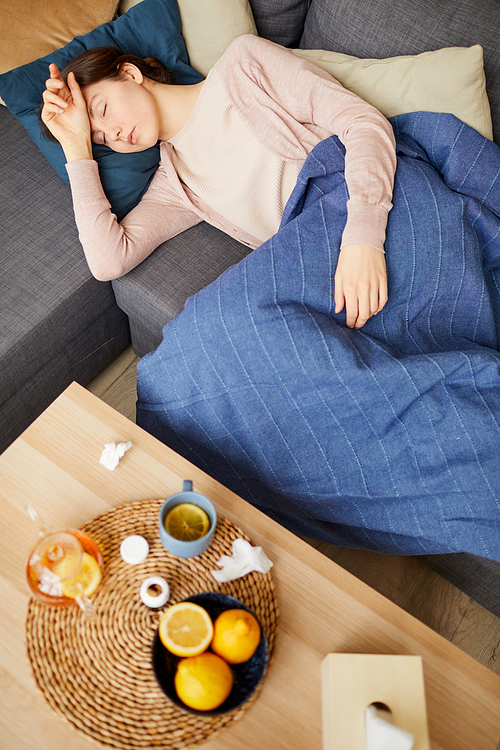 Sick woman lying on sofa with table near by with tea fruits and pills she has a headache