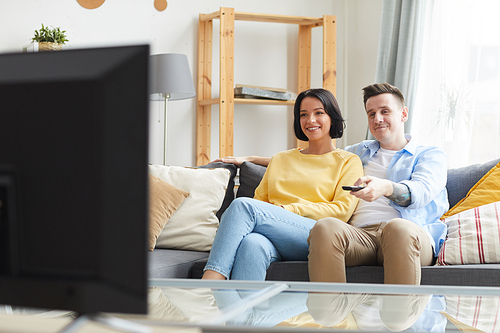 Young smiling couple sitting on sofa and watching TV in the living room at home