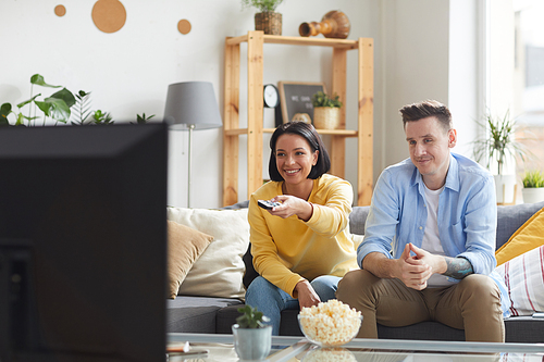 Happy young couple sitting on sofa and spending their leisure time at home they watching TV