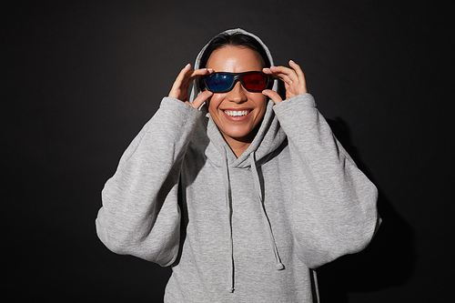 Portrait of young happy woman in hoody wearing 3D glasses and watching film isolated on black background