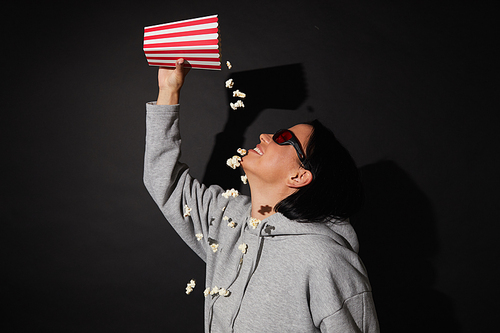 Young woman in 3D glasses eating popcorn while standing over black background